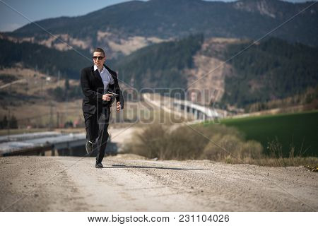 Agent In A Suit Holding A Gun And Running At A Highway Construction Site In James Bond Movie Style.