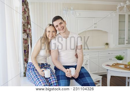 Loving Happy Couple In Their Pajamas In The Morning Eating Breakfast In The Kitchen.