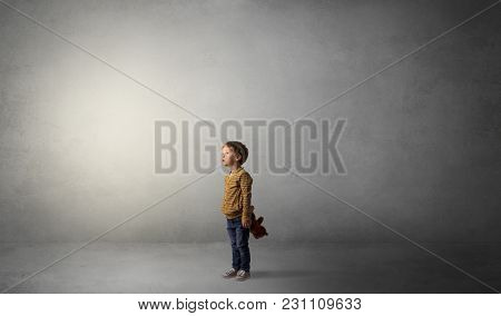 Little waggish kid staying alone in a big empty room with his plush