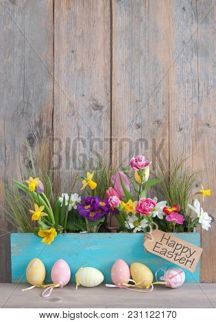 Spring Flowers In A Wooden Pot With Row Of Easter Egg