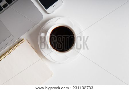 Flat Lay On White Wooden Workspace With Laptop Computer, Cell Phone Gadget And Black Coffee.