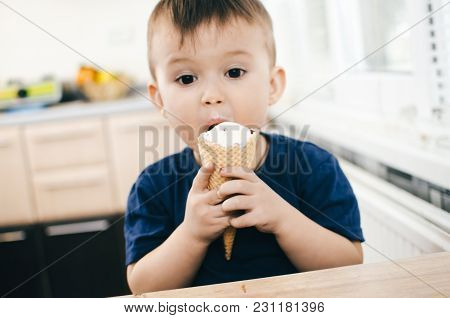 A Child In A Dark-blue T-shirt In The Bright Kitchen Eating A Waffle Ice Cream Cone In The Summer Ho