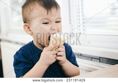 A Child In A Dark-blue T-shirt In The Bright Kitchen Eating A Waffle Ice Cream Cone In The Summer Ho