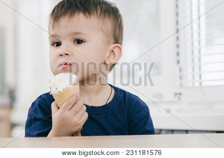 A Child In A Dark-blue T-shirt In The Bright Kitchen Eating A Waffle Ice Cream Cone In The Summer Ho