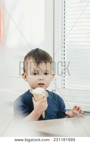 A Child In A Dark-blue T-shirt In The Bright Kitchen Eating A Waffle Ice Cream Cone In The Summer Ho