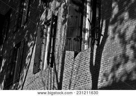 Black And White Photo Of A Building With Black Windo Shutters Open, Sun Falling On The Side Of The B