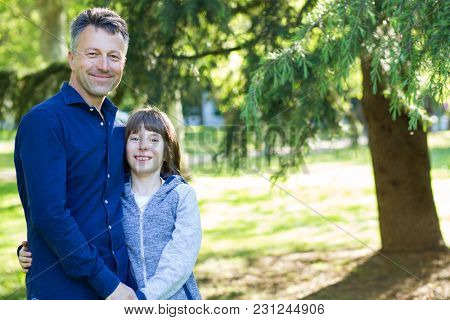 Handsome middle-aged man in park with his son. Attractive mid adult male model posing outddor with teen boy.