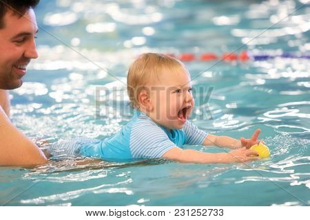 A father helps is infant daughter during swimming lessons in the pool.