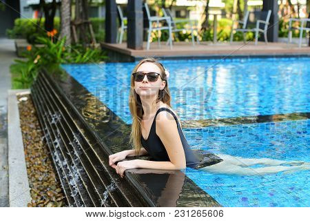 Young Woman Relax In Swimming Pool, Looking At Camera Wearing Sunglassses And Enjoy Weather In Tropi