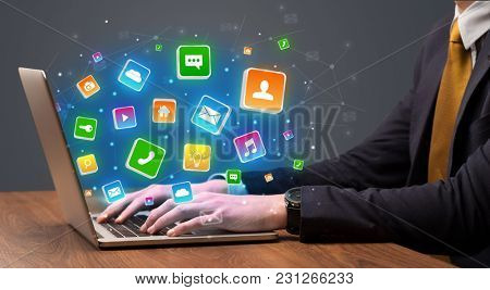 Businessman hand typing on laptop with flying application icons around