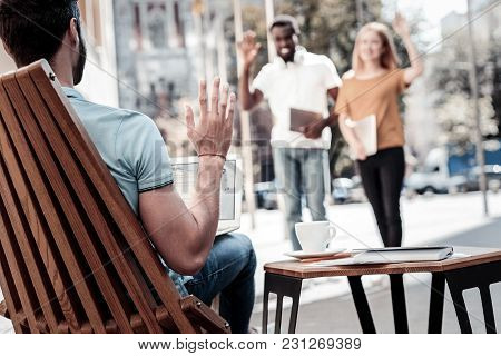 Hello There. Selective Focus On A Millennial Gentleman Relaxing In A Chair And Waving Too His Collea