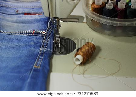 On The Table Of The Sewing Machine Lie Denim Fabrics, Close-up, Next To The Thread And Scissors.