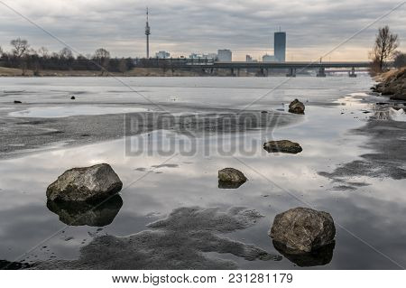 Frozen River, Stones Lying On The Ice And High Buildings In The Background, Vienna Austria