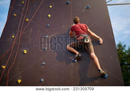 Sporty Man Practicing Rock Climbing In Climbing Gym Artificial Rock Training Wall Outdoors. Young Ta