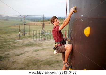 Sporty Man Practicing Rock Climbing In Gym On Artificial Rock Training Wall. Young Talanted Climber 