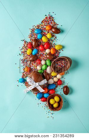 Easter Chocoalte Eggs And Sugar Multicolored Sprinkles On Blue Background With Copy Space. Top View