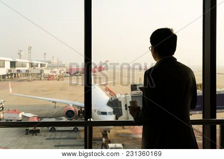Young Businessman Stand At Terminal In Internatianal Airport During Sunset And Chatting On The Phone