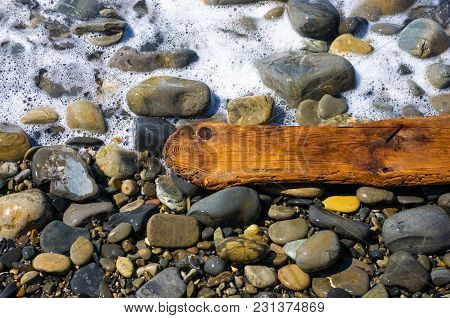 Driftwood, Washed Up By The Sea On A Pebble Beach On A Warm Summer Day