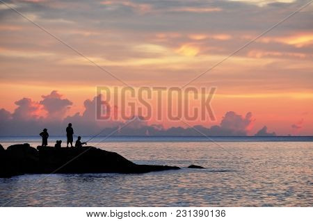 Peole Are Fishing On The Rocks Near The Ocean  At Sunset