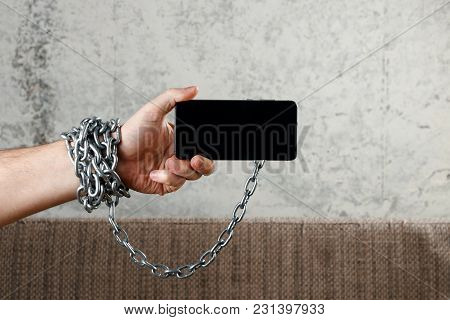 Close-up, The Man's Hand Is Tied With A Chain To The Smartphone. The Concept Is Dependent On Technol