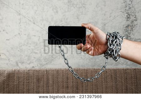 Close-up, The Man's Hand Is Tied With A Chain To The Smartphone. The Concept Is Dependent On Technol