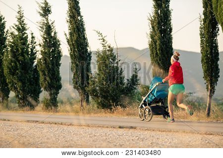 Running Mother With Child In Baby Stroller Enjoying Sunset And Mountains Landscape. Jogging Or Power
