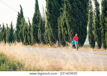 Running Mother With Child In Baby Stroller Enjoying Sunset And Mountains Landscape. Jogging Or Power