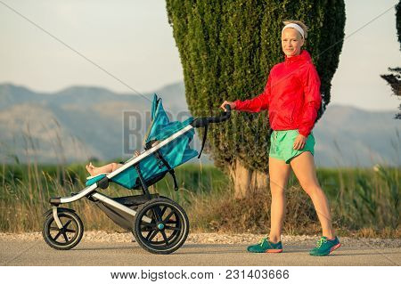 Mother With Child In Baby Stroller Enjoying Summer Sunset And Mountains Landscape. Jogging Or Power 