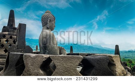 Amazing view of ancient Borobudur Buddhist temple with meditating Buddha statue carved from dark stone against blue sky on background. Great religious architecture. Magelang, Central Java, Indonesia