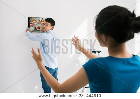 Young Vietnamese Couple Hanging Photo On Wall In The Room