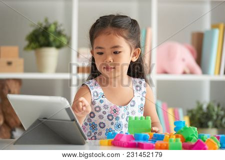Little Girl Following Tutorial On Tablet Computer When Building From Plastick Bricks