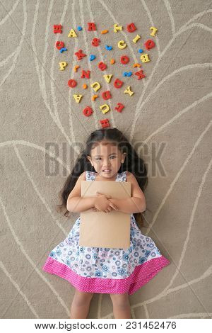 Cheerful Little Girl Lying On The Floor With Plastick Letters Near Her Head