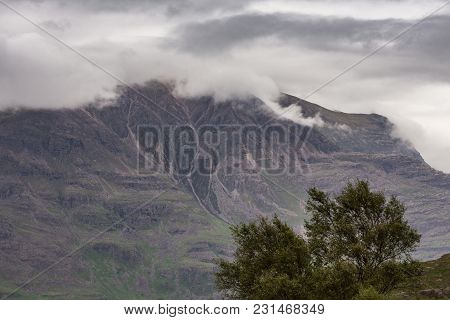Annat, Scotland - June 10, 2012: Closeup Of Massive Brown-green Mountain Wall With Top In Clouds. Gr