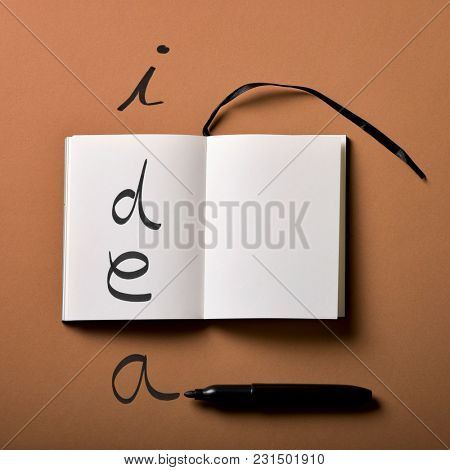 high angle view of an open notepad and a black marker pen, and the worid idea written with it