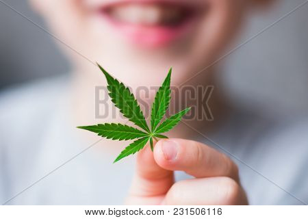 Smiling Kid Child Holding A Hemp Leaf. Concepts Of Using Marihuna For Medicinal Purposes For Childre