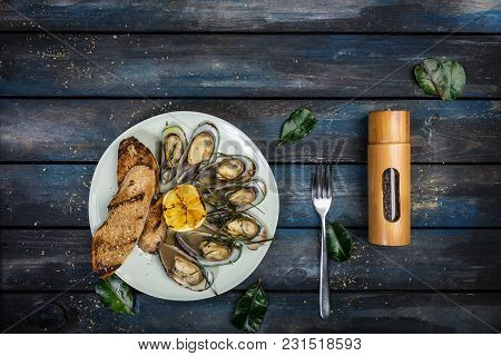 Mussels And Bread Toasts On On A White Plate. Served With Half Grilled Lemon, Fork And Leaves Of Kaf