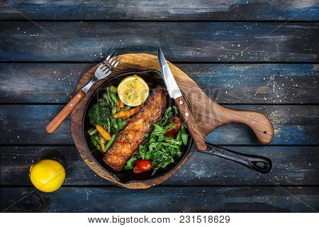 Grilled Salmon Fillet In A Frying Pan, Vegetables, Arugula With A Lemon. On The Cutting Board And Wo