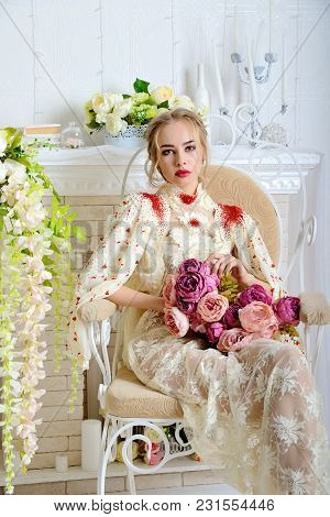 Beautiful Girl Sitting And Posing On A Vintage Stool In The Studio With A Bouquet Of Flowers In His 