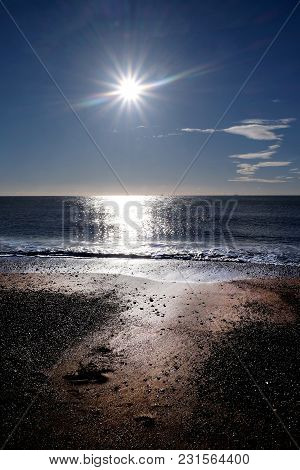 Sun In Blue Sky With Sunbeam In The Centre Casting Long Highlight From The Sun Accross The Sea And T