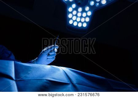 Doctor's Hand Holding A Scalpel Knife Surgeon Work With Patient On Bed In Dark Operating Room At Hos