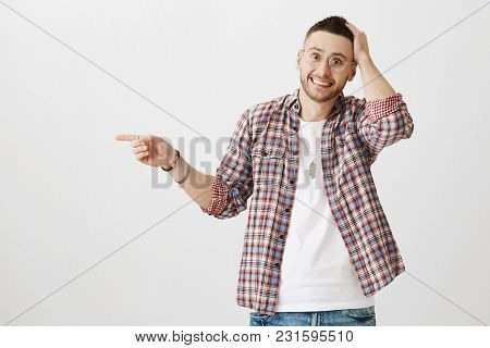 Confused Embarrassed Attractive Man In Glasses Pointing Left While Holding Hand On Head, Looking Sur