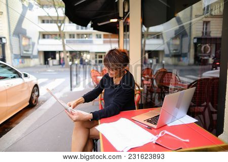 Woman Sitting At Table Of Street Cafe Skimmed Through New Newspaper. Female With Short Haircut Dress