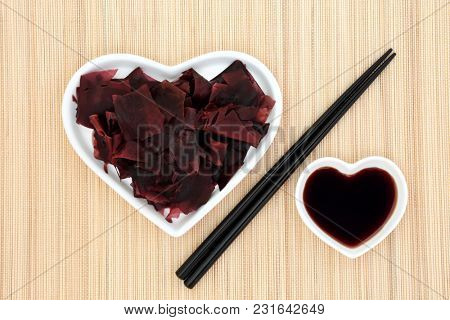 Dulse seaweed health food in a heart shaped dish with low sodium soy sauce and chopsticks on bamboo background. Super food very high in minerals and protein. 