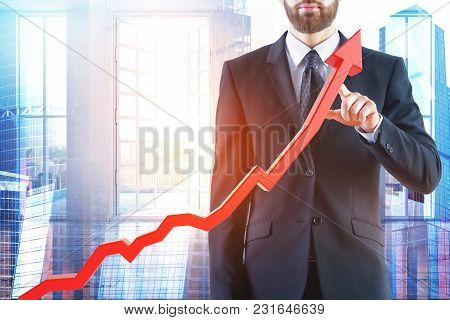 Businessman Pointing At Abstract Upward Red Business Chart Arrow On City And Background. Startup And
