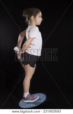 Little Caucasian Girl In On One Leg Position Staing On Balance Board. Photo On Black Background