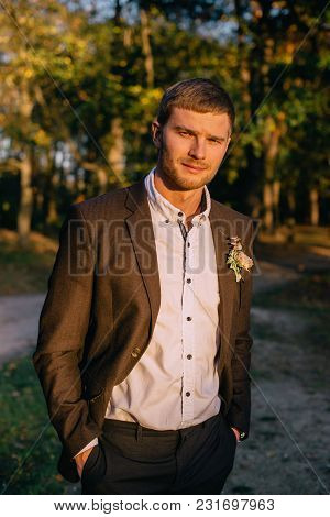 Young Groom Looks At Camera And Smiles Against Nature Background