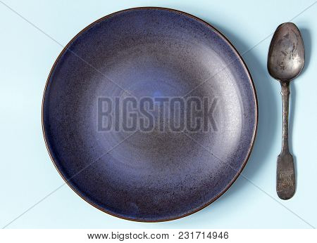 Empty Ceramic Round Plate And Spoon On Background In Blue Pastel Colors.  Top View With Copy Space.