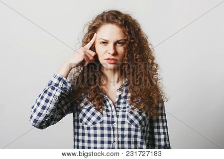 Serious Beautiful Curly Woman Keeps Finger On Temple As Tries To Remember Some Details, Dressed In B