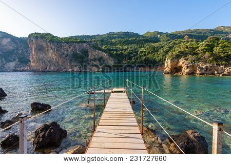 Wooden Pier In Paleokastritsa Bay With Sand And Crystal Sea Water. Corfu Island, Greece.