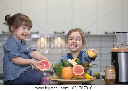 Two Cute Little Girls Cooking Fresh Juice In The Kitchen, The Concept Of A Healthy Baby Food And A H